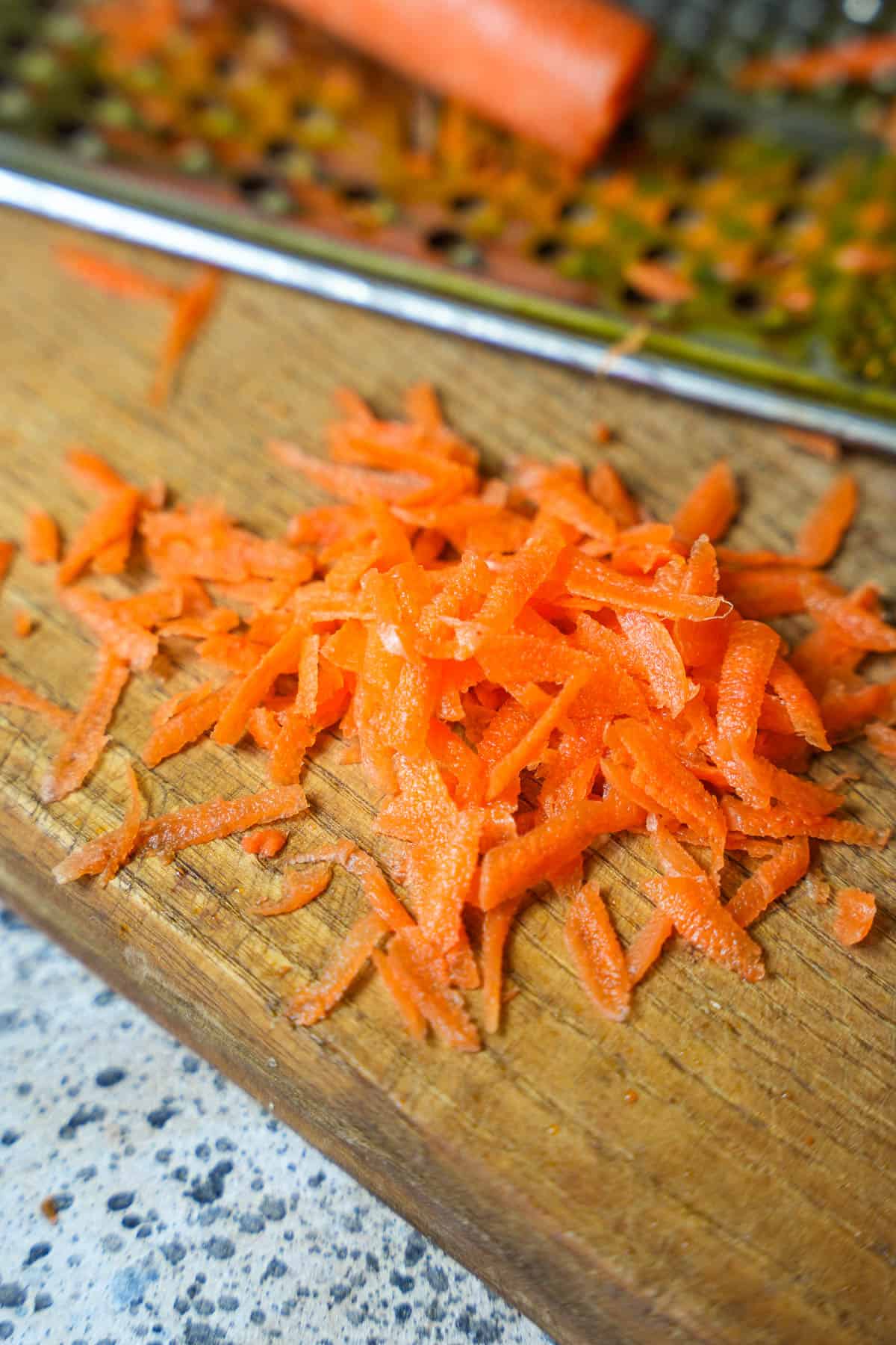The carrot is shredded on a wooden board next to a grater.