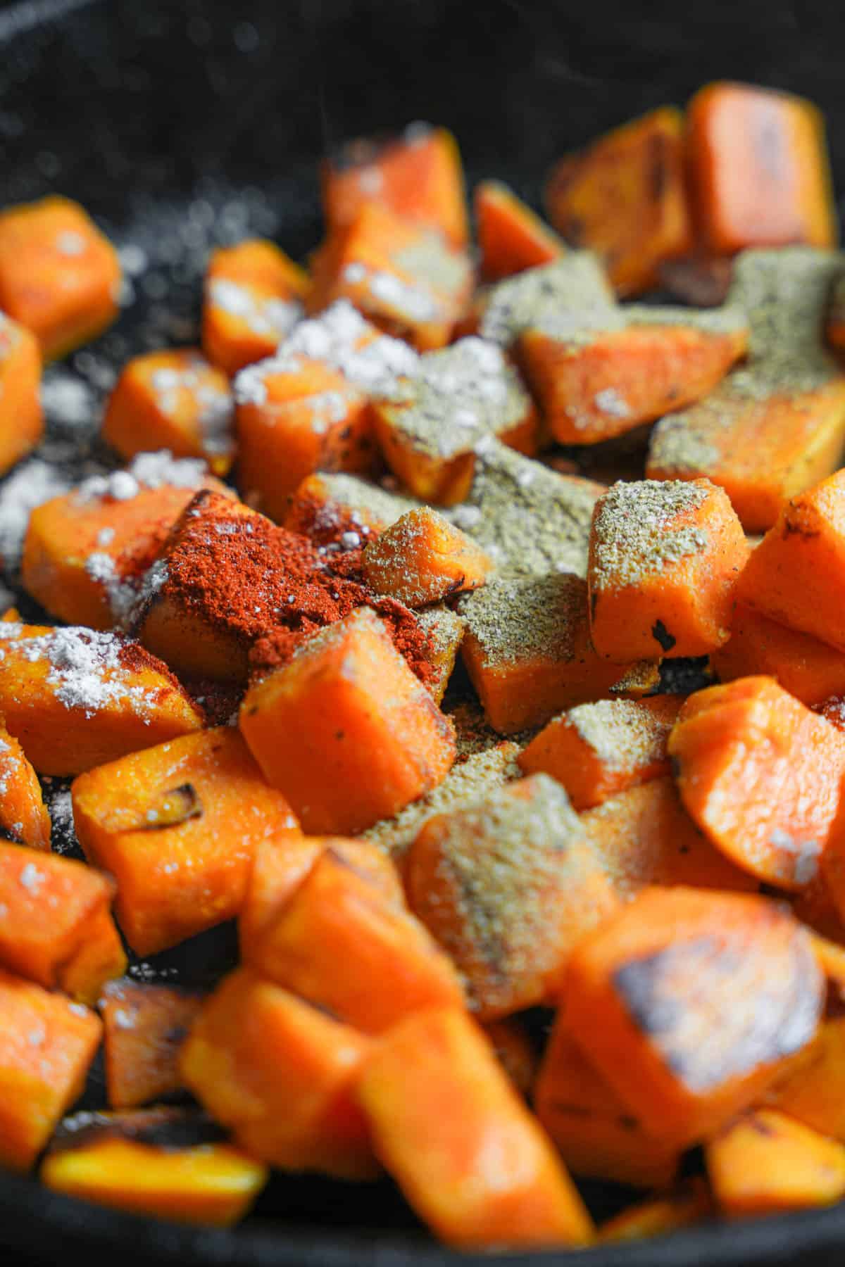 Chaat masala, chili powder and black salt are added to the cooking sweet potatoes.