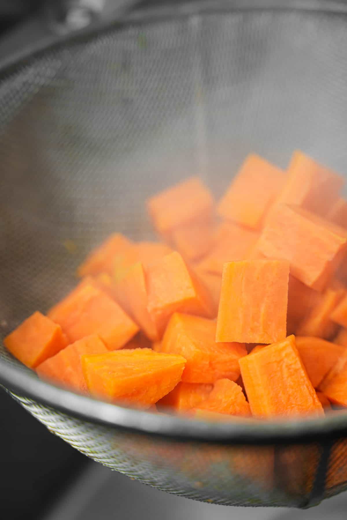 Par-cooked sweet potatoes are drained in a wire mesh strainer.