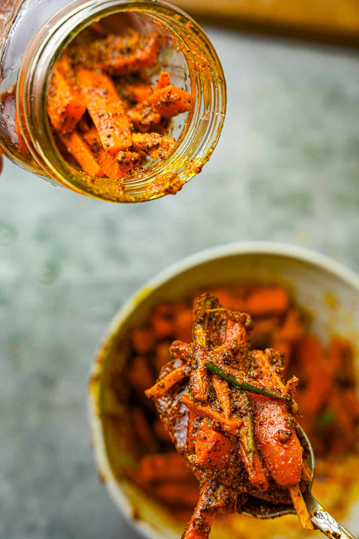 Carrot pickle is loaded into a jar with a metal spoon.
