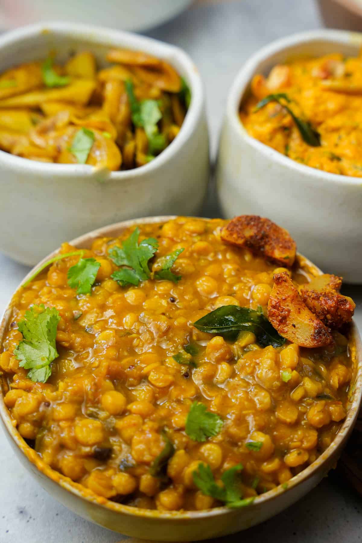 chana dal garnished with cilantro with parwal and curry on a table.