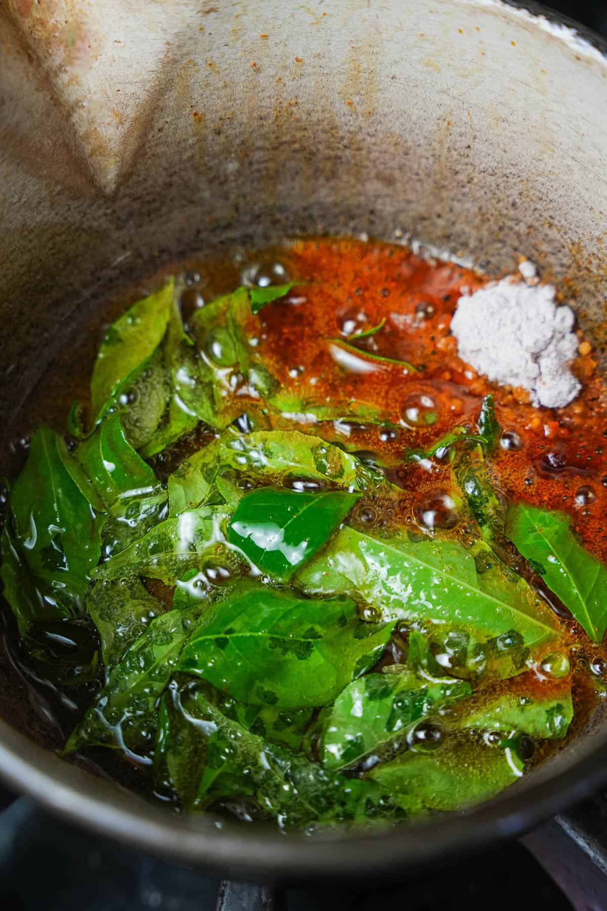 a frying pan filled with frying curry leaves and spices.