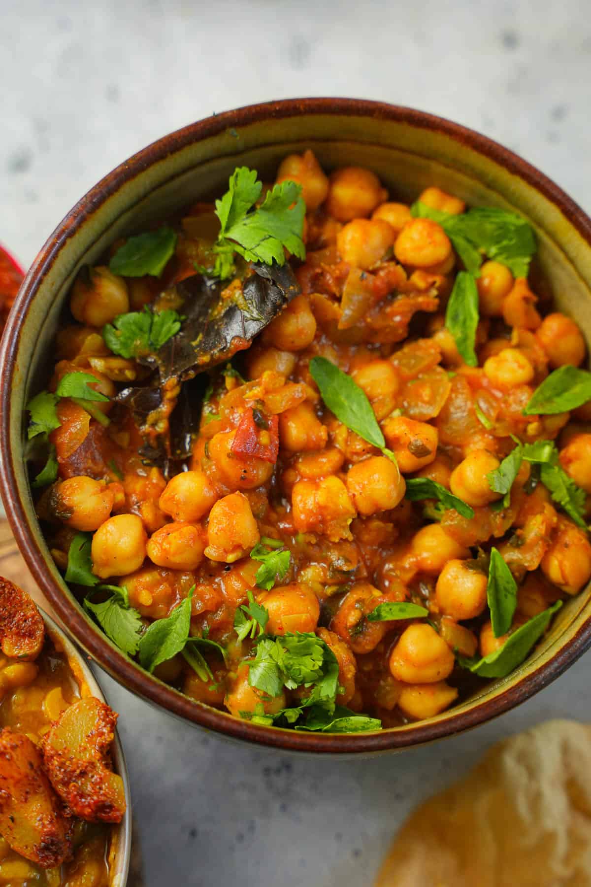 a bowl of chana masala with tomatoes and spices garnished with methi and cilantro.