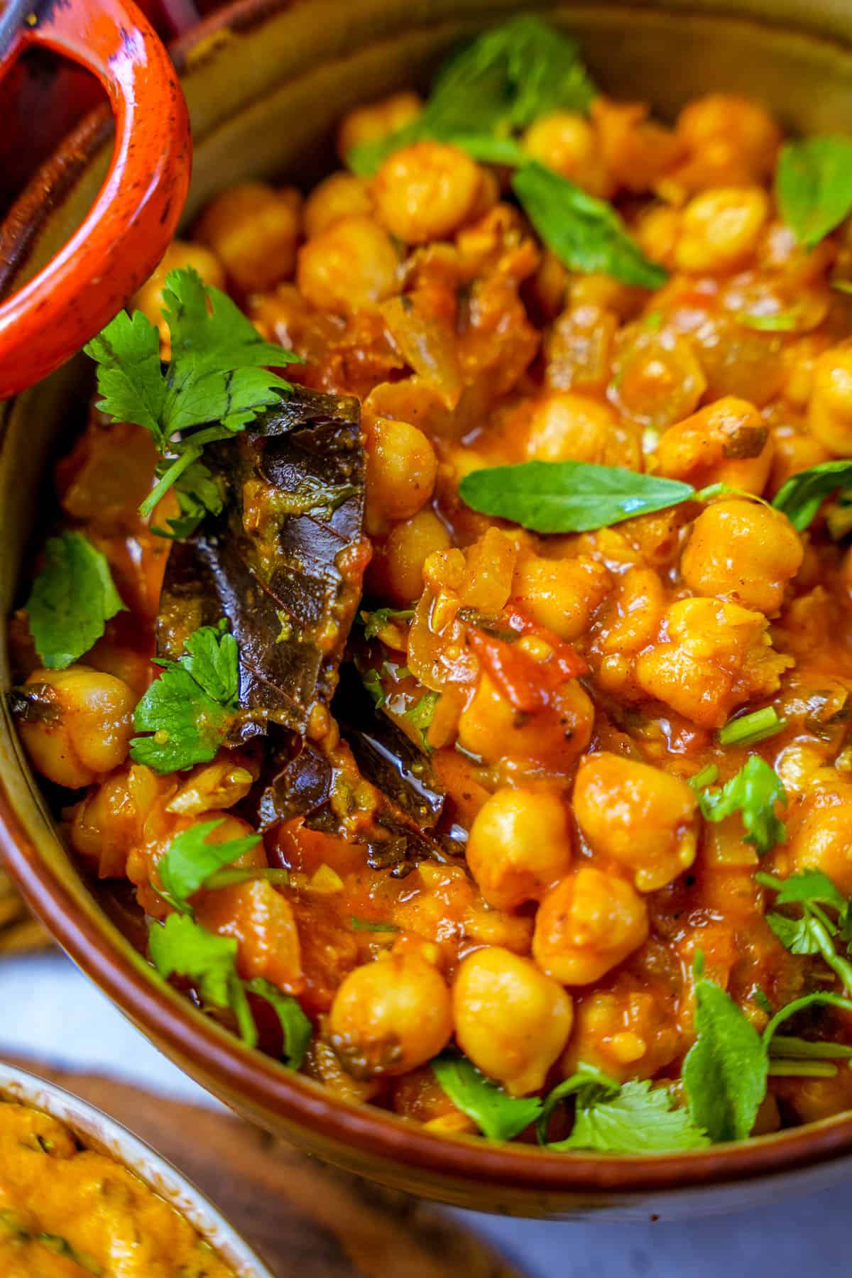 a bowl of chana masala garnished with methi and cilantro on a table.