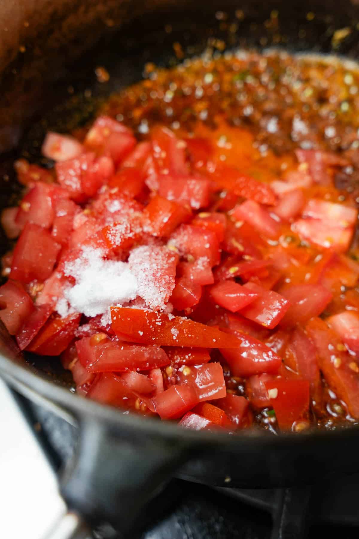 tomatoes and salt are added to the cooking spices and veggies in the pan.
