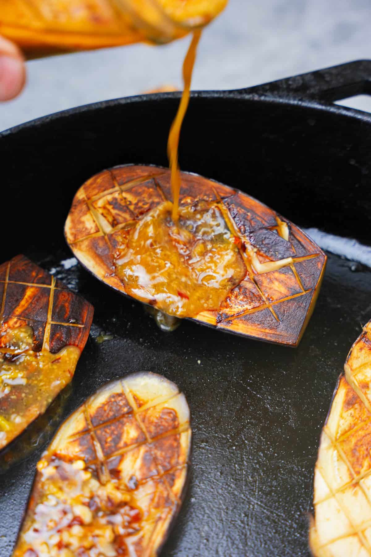 Miso glazed is poured onto seared eggplant in a cast iron skillet.