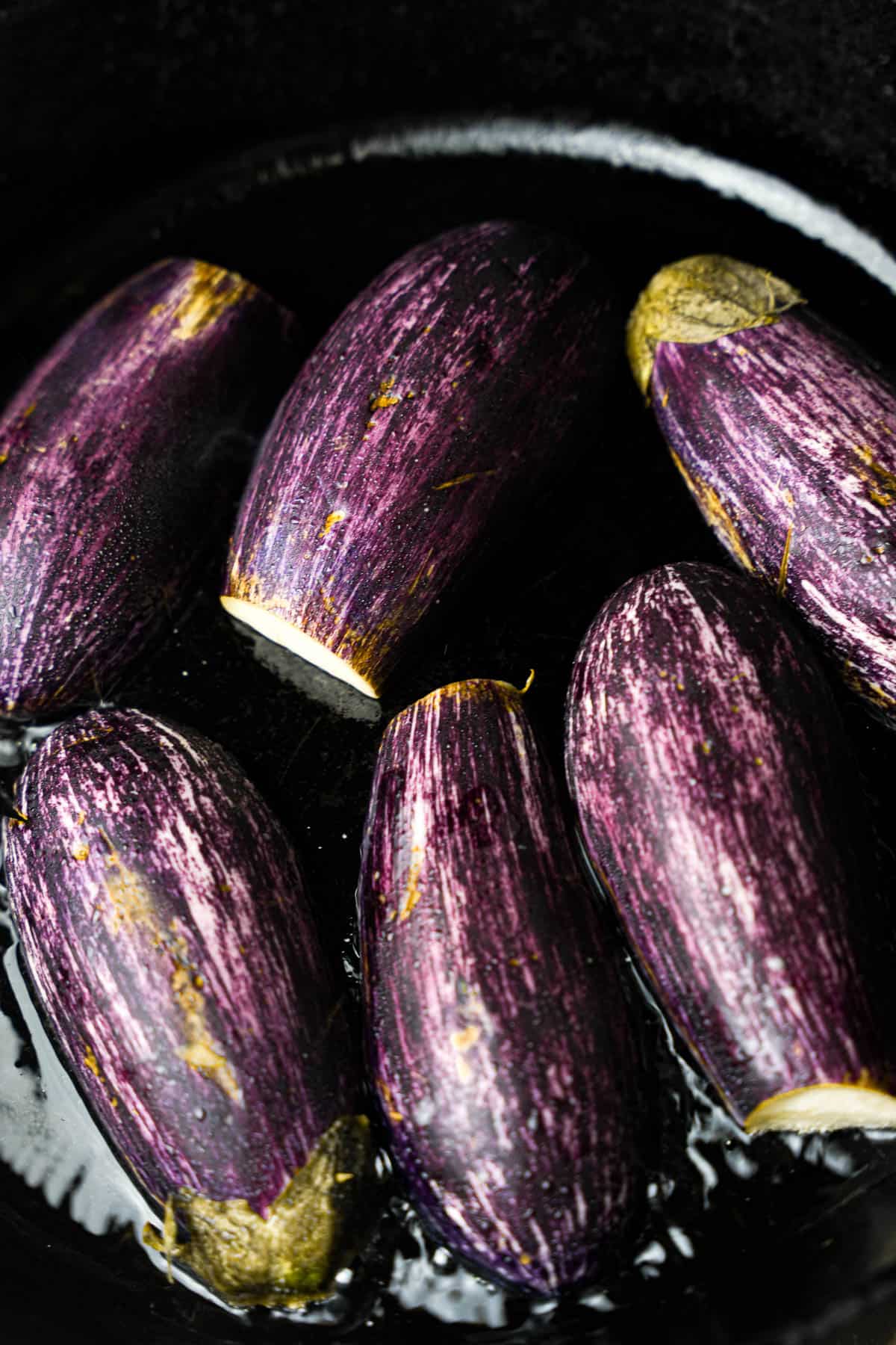 eggplants cooking cut side down in hot oil in a pan on a stove top.