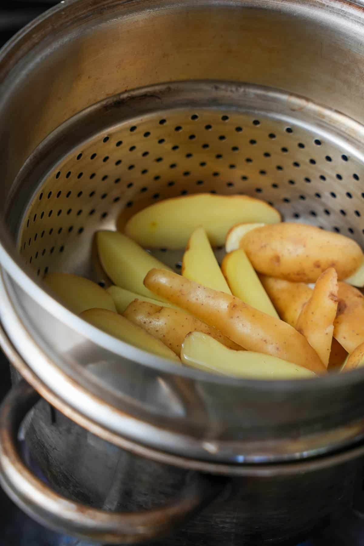 Potatoes steaming in a metal steamer on a stove.