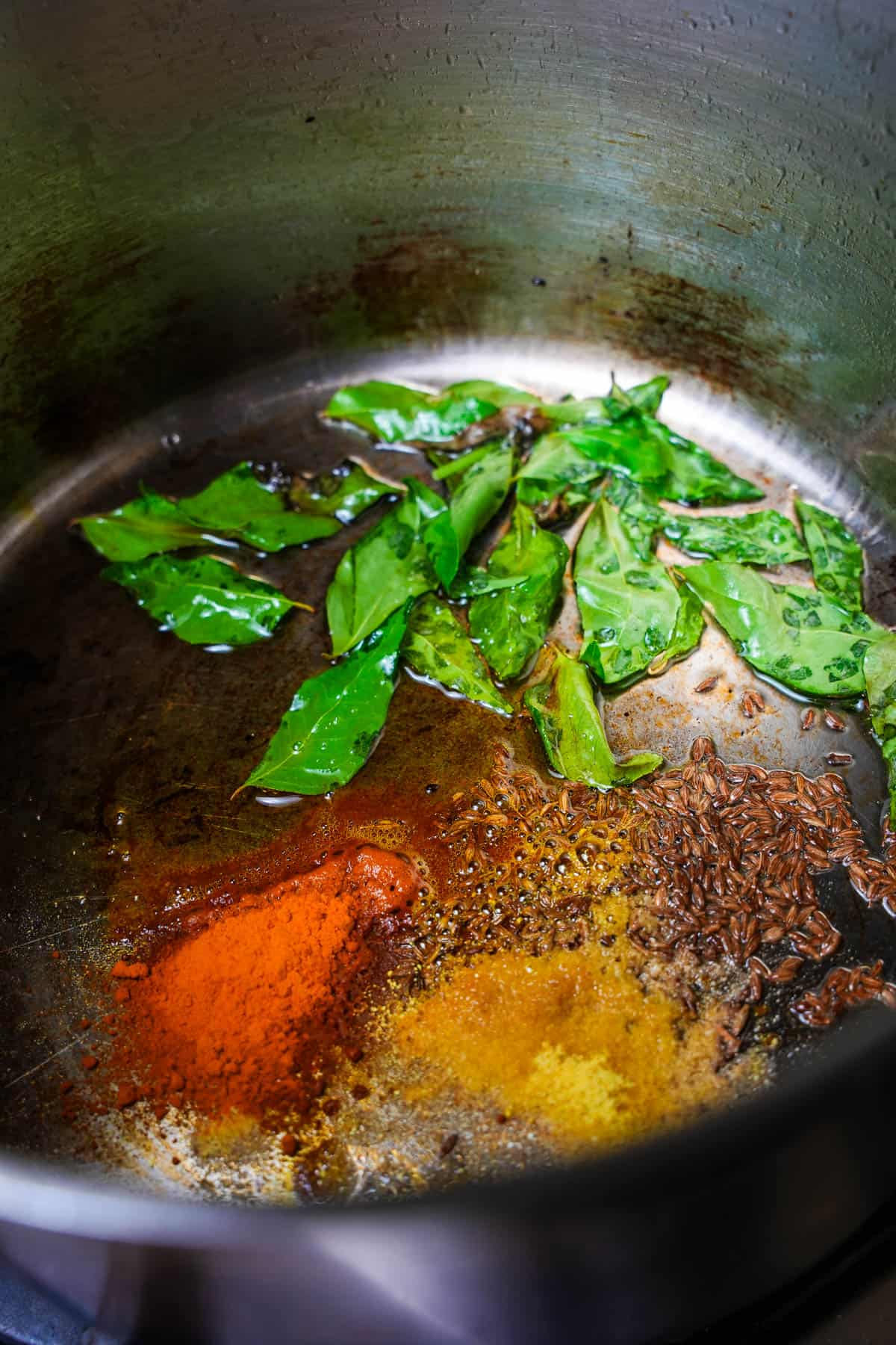 A pan with spices and curry leaves in it on a stove top.