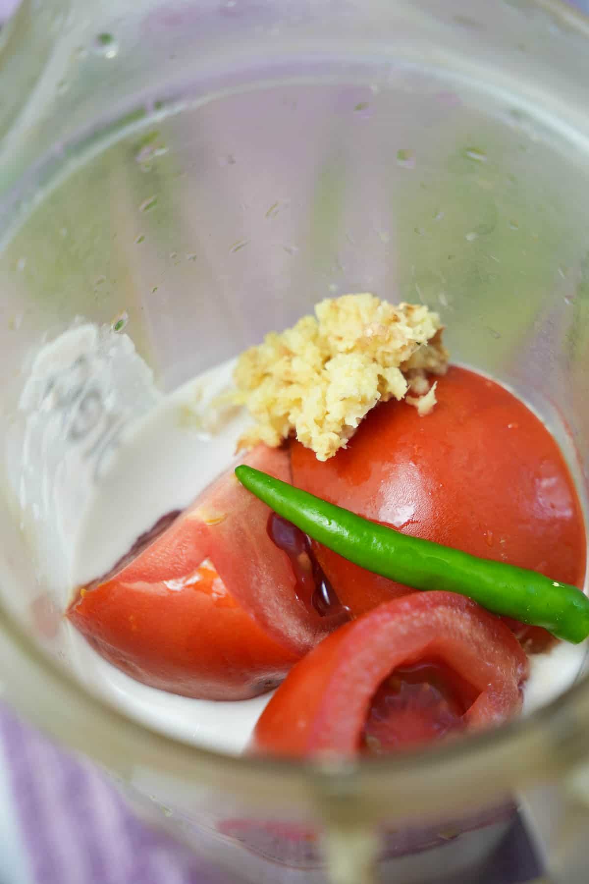 A blender filled with tomatoes, chilies, cashews and coconut milk.