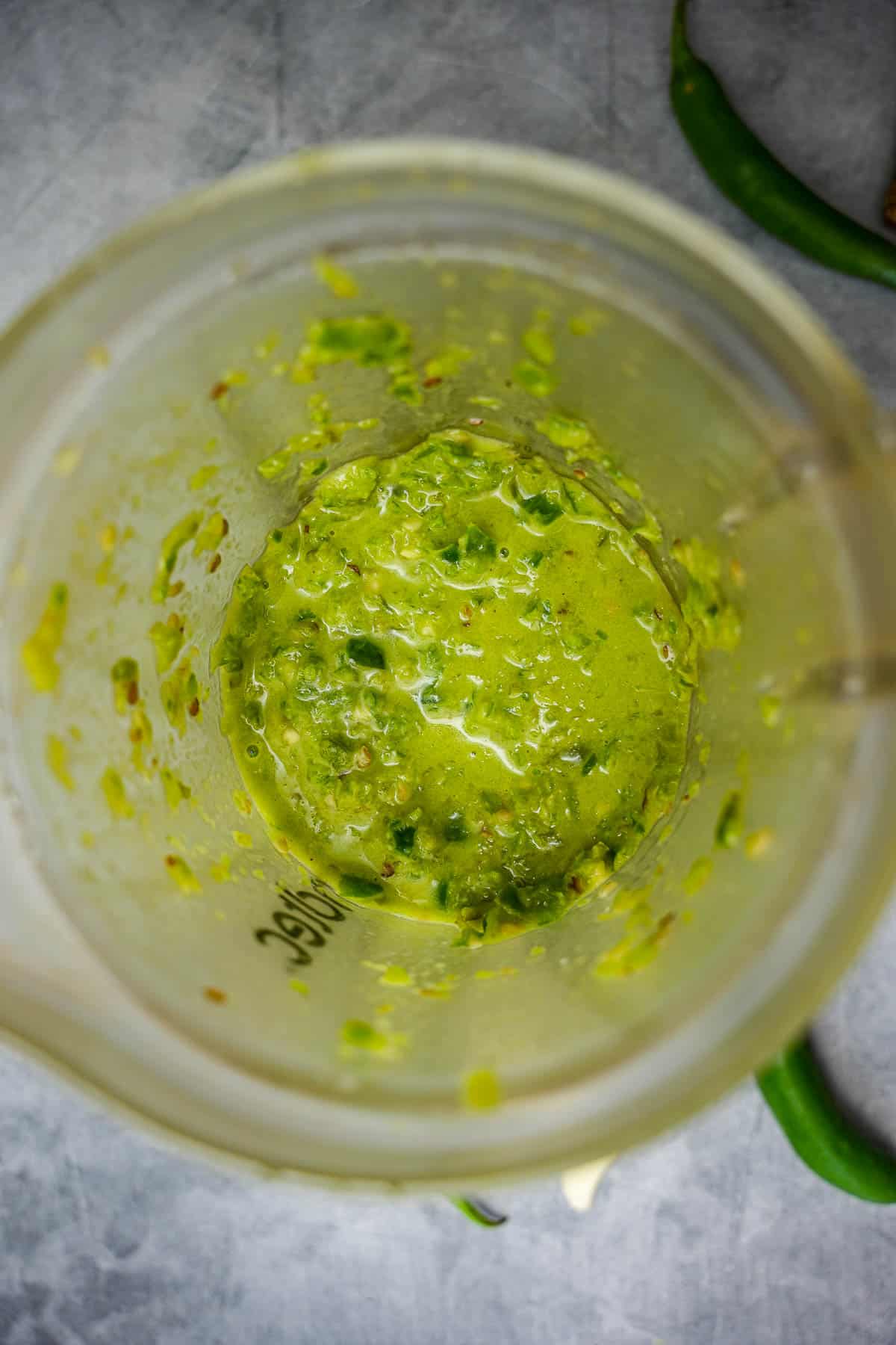 a blender filled with green shatta sauce. Garlic and peppers on the table.