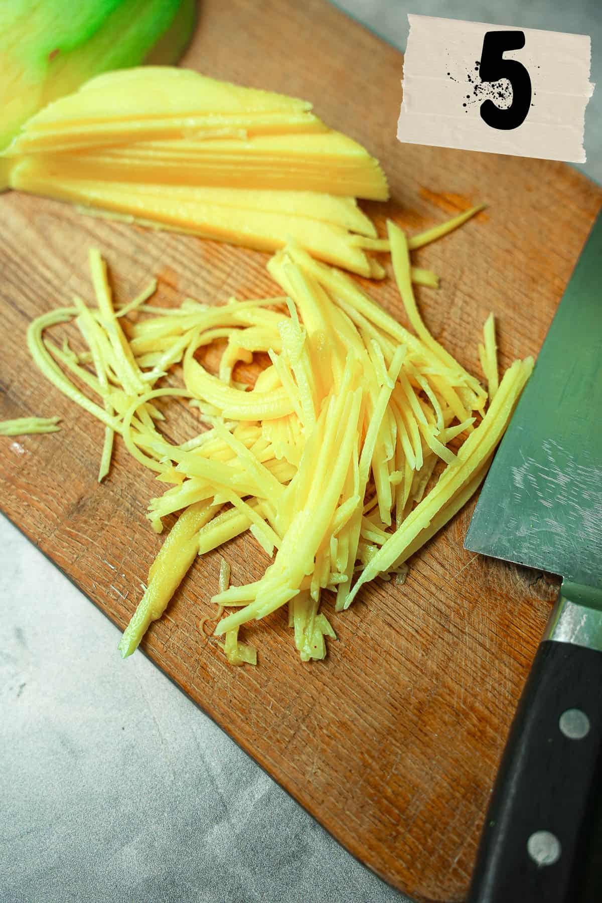 Julienne cut green mango with a knife on a cutting board.
