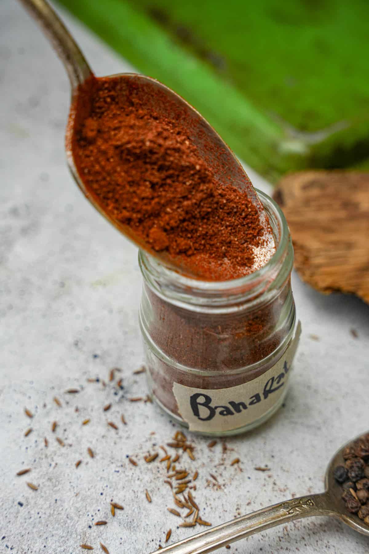 Spices being loaded into a labeled jar with a spoon.