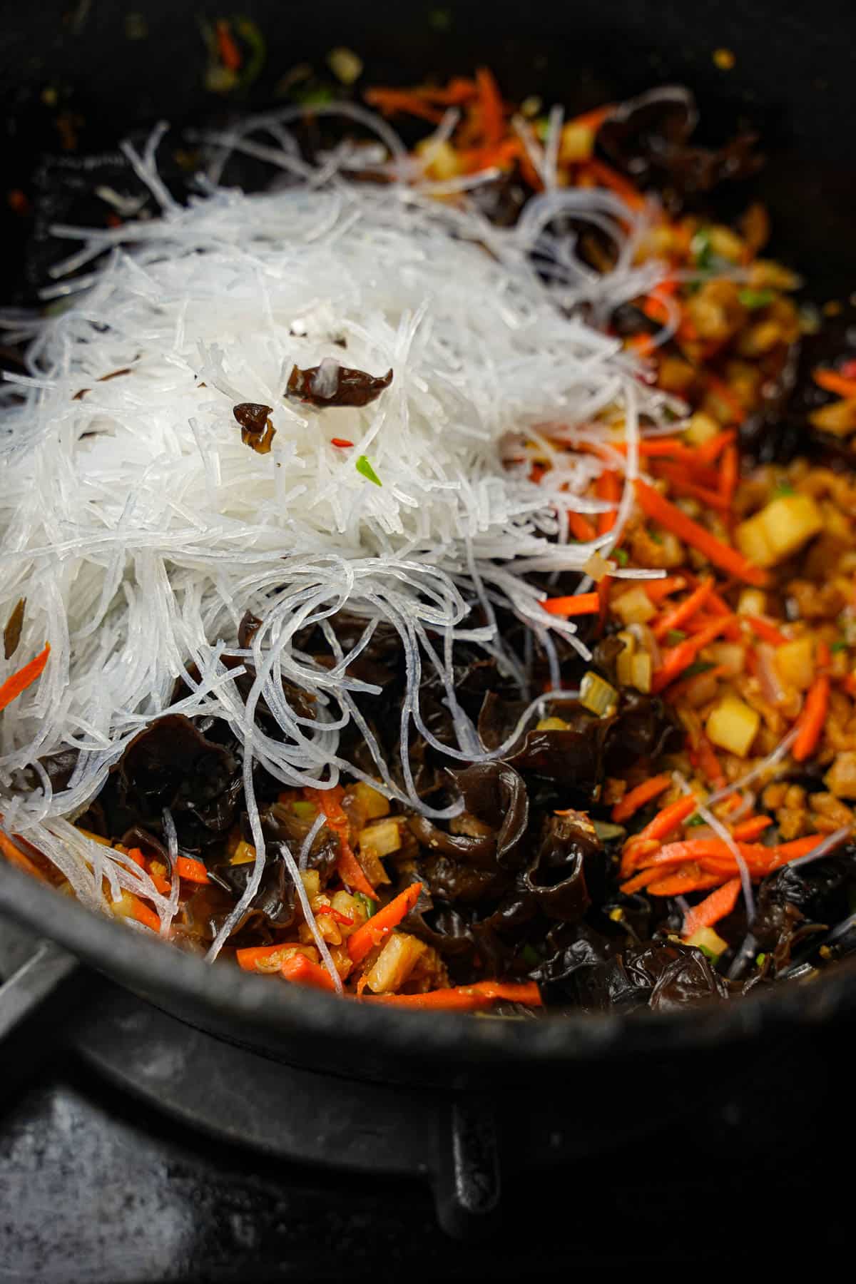 Black fungus, sauces, and noodles are added to the sauteeing veggies in a pan.