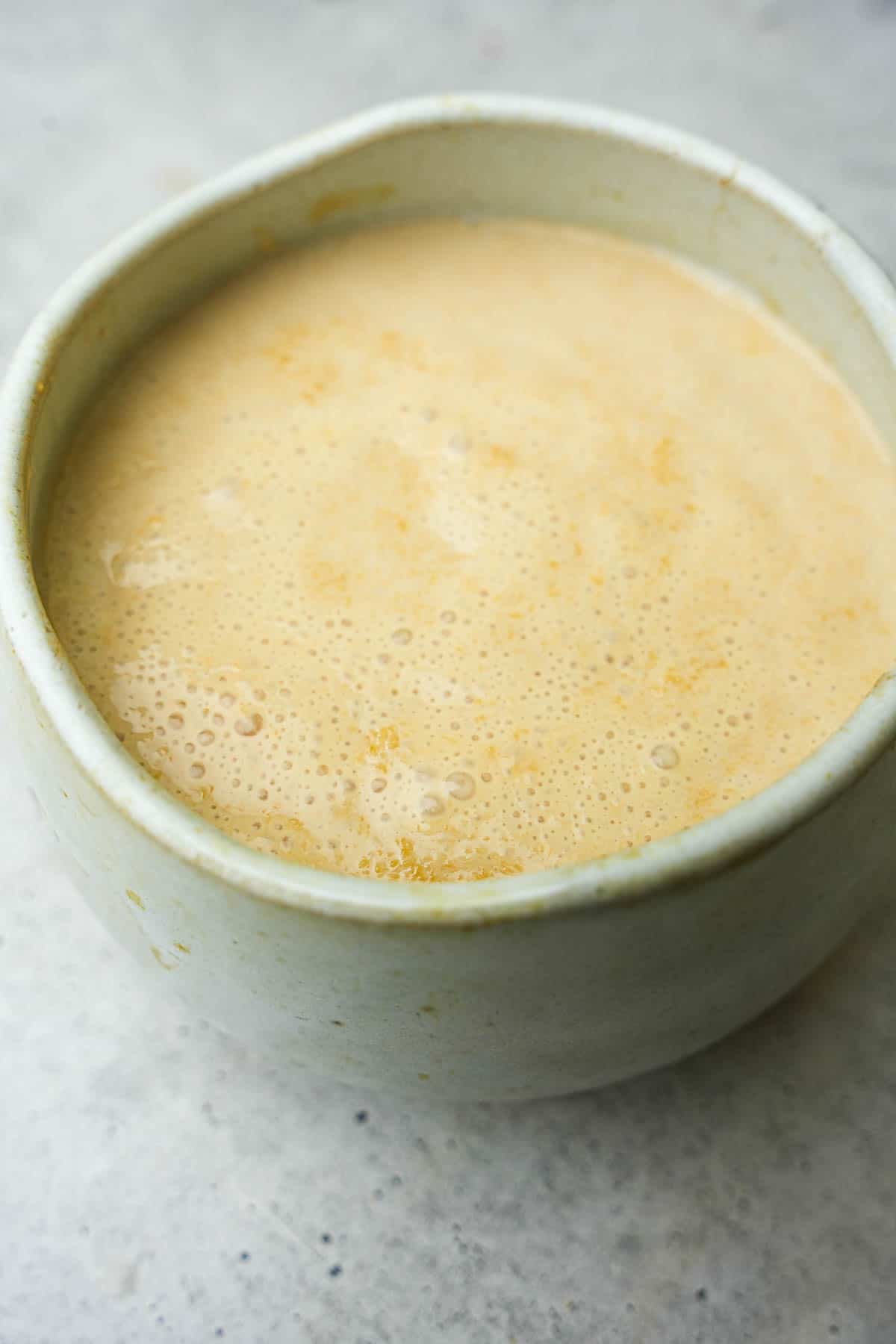 A bowl of yeast, proofing on warmed plant-based milk on a table.