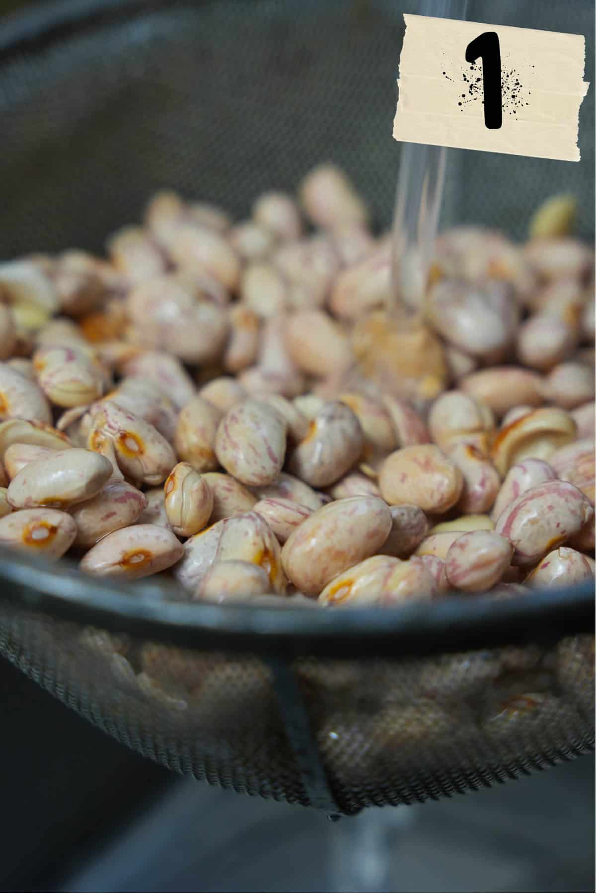 Soaked dried borlotti beans are strained and rinsed in a wire mesh strainer.