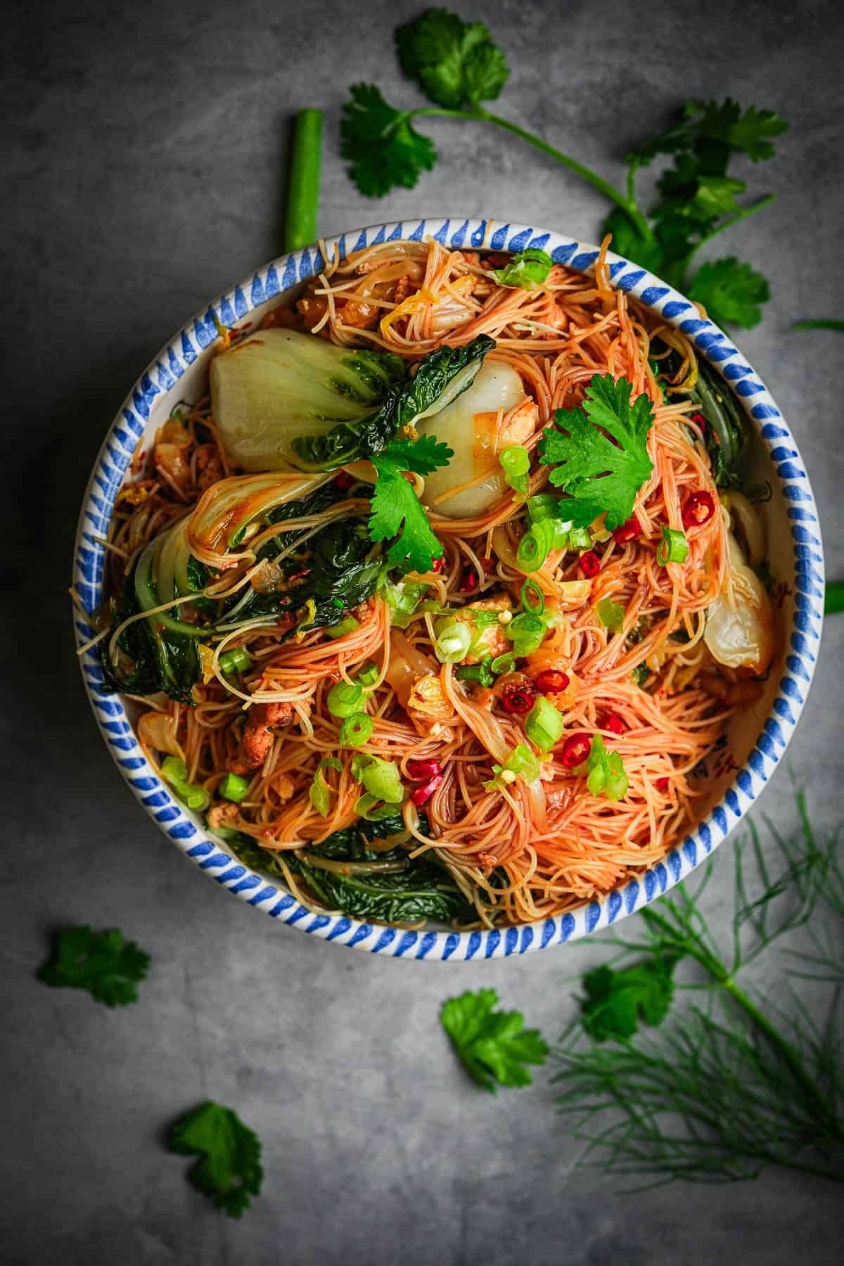 A bowl of bihun goreng with vegetables and herbs.