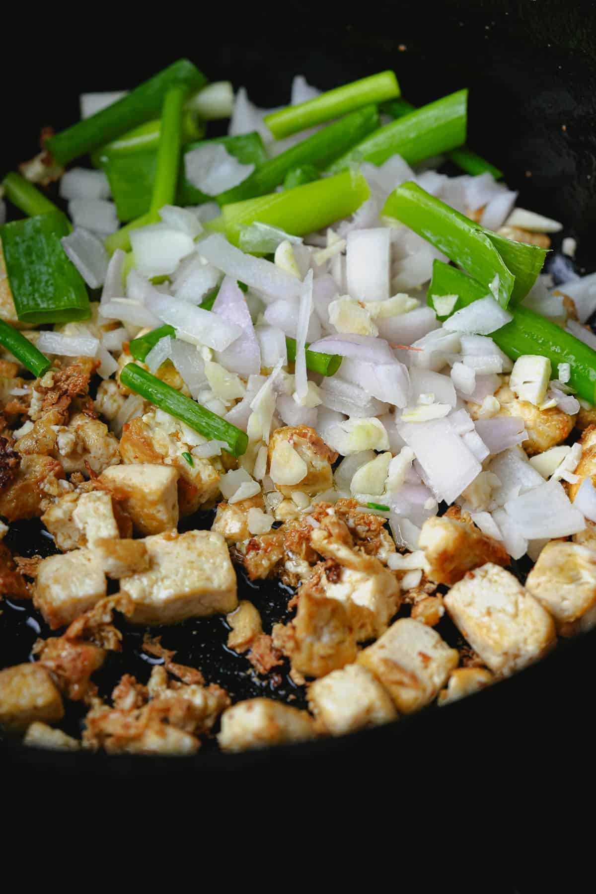 A frying pan with shallots, garlic, scallions and tofu in it.