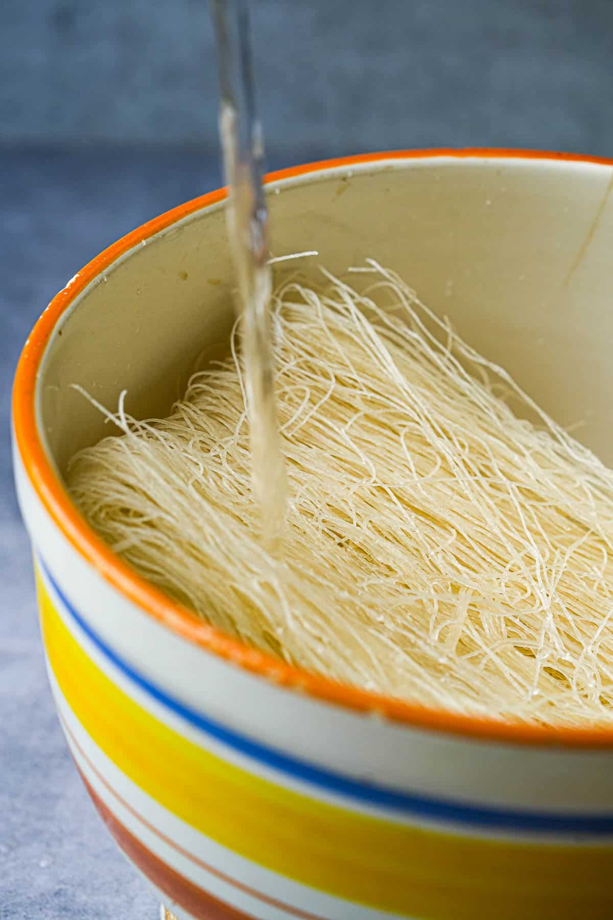 A ceramic bowl of noodles with water being poured into it.