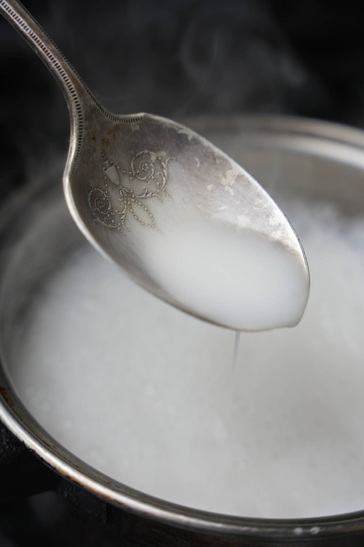 A spoon is stirring coconut milk in a pan.
