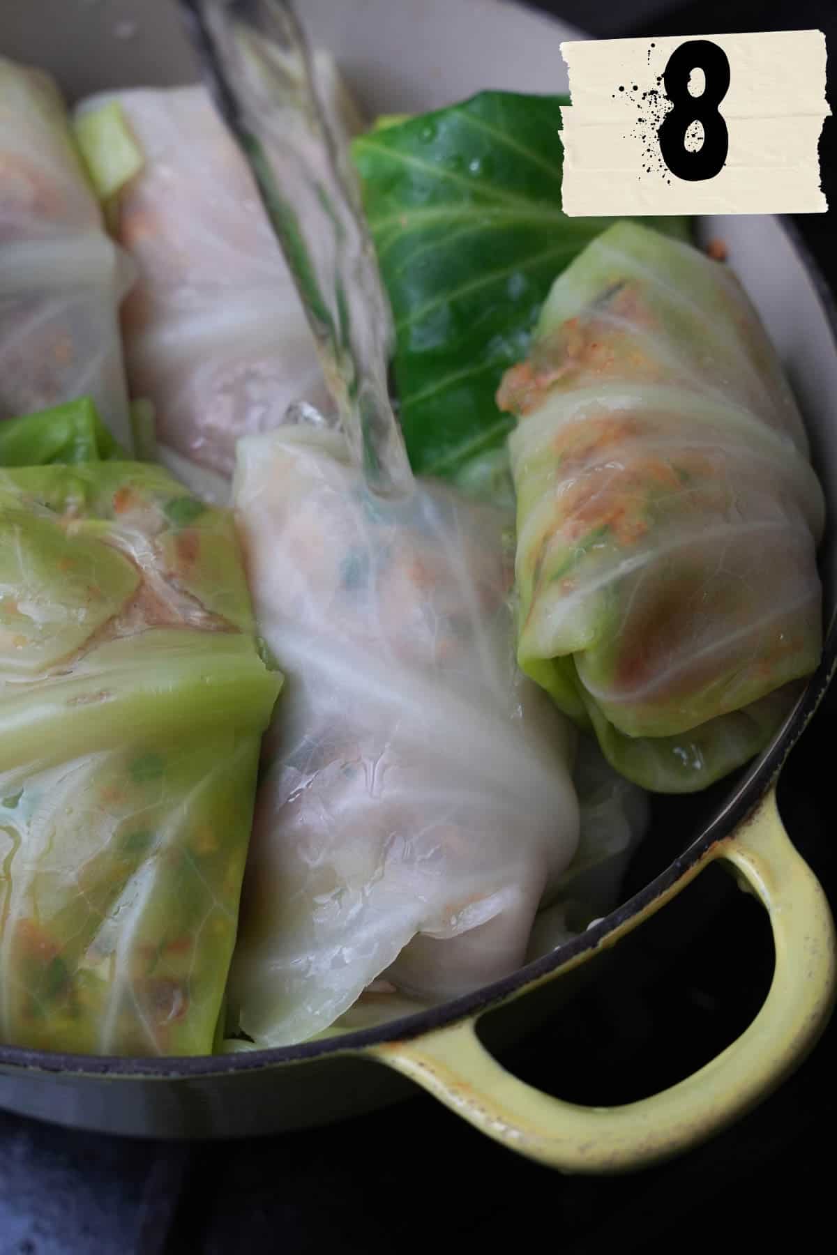 Hot water is pored over the stuffed cabbage in a yellow pot.