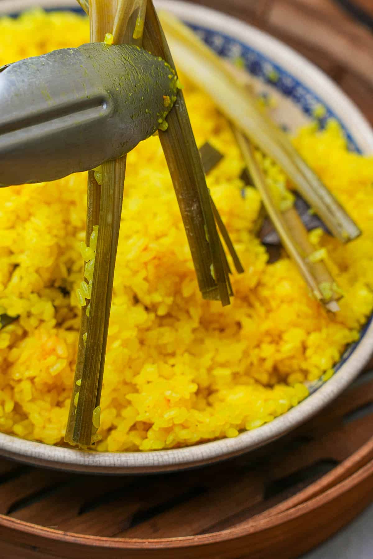 A plate of yellow rice with a pair of tongs removing pandan leaves from it.