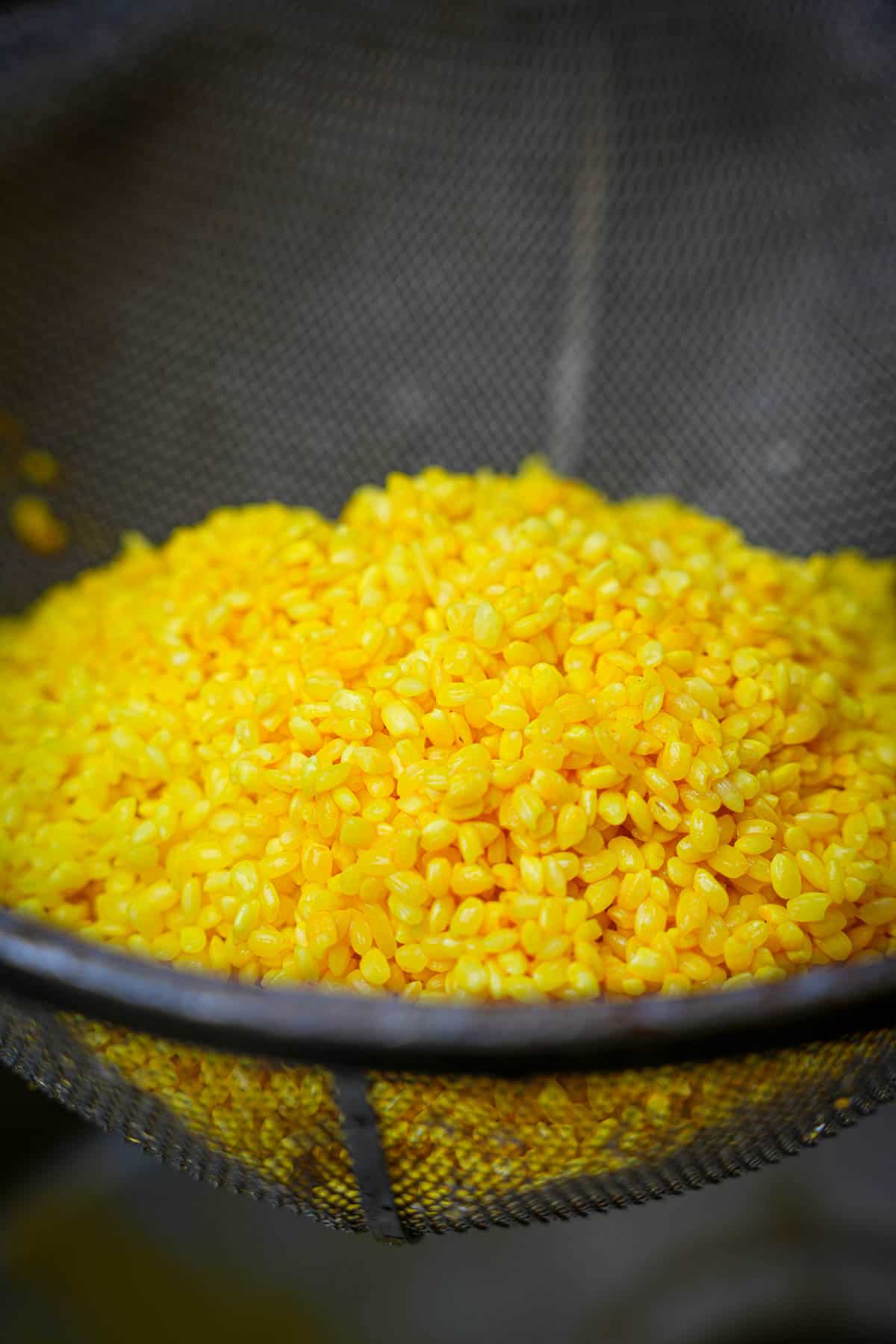 Yellow rice draining in a mesh basket.