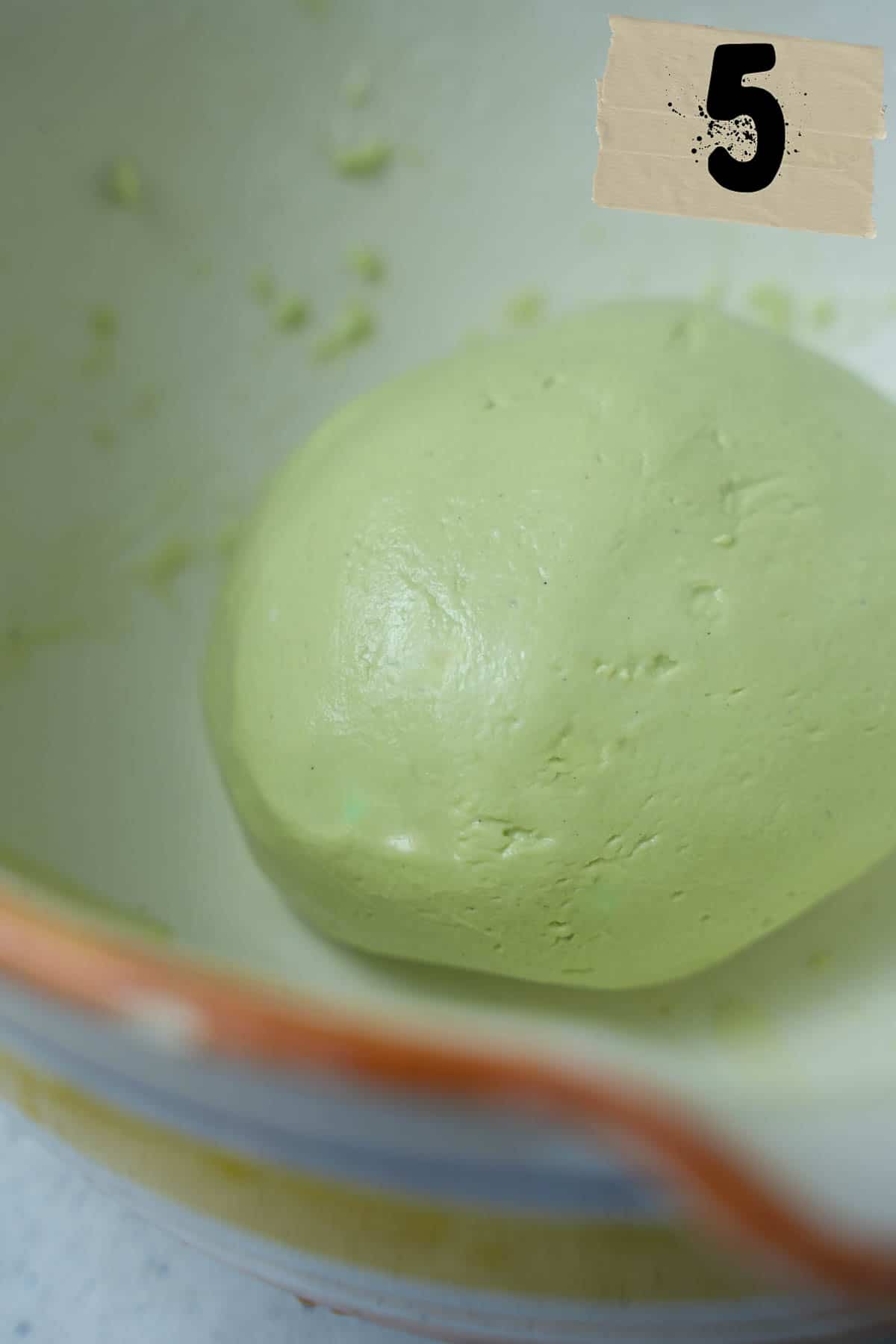 A bowl of green dough rolled into a ball.