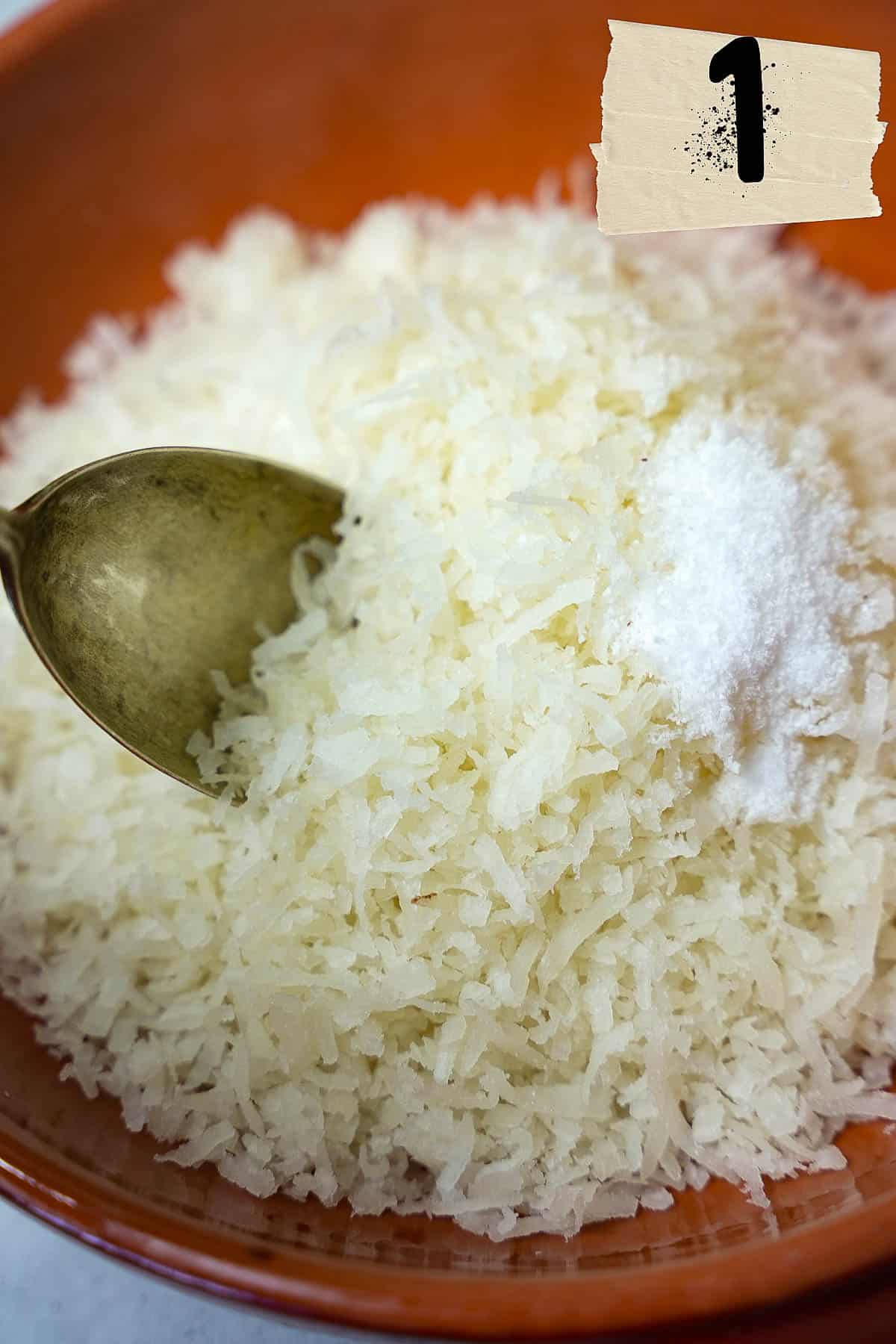 A bowl of shredded coconut and salt with a spoon in it.
