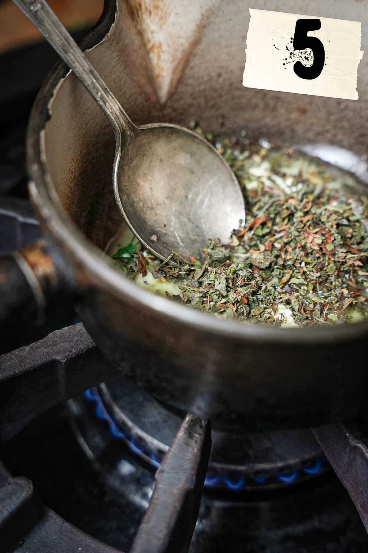 Dried mint is stirred into melted vegan butter in a pot with a spoon.