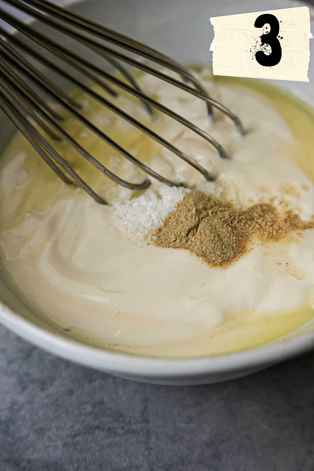 A whisk combines yogurt and other ingredients in a white ceramic bowl.
