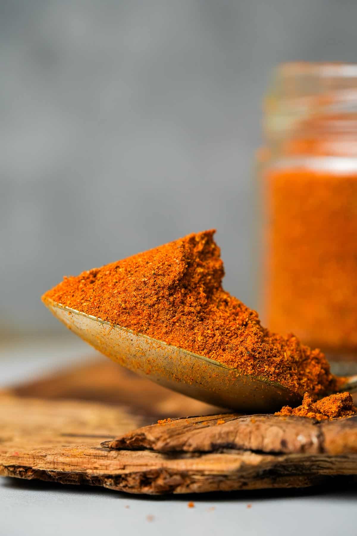 A spoonful of achar masala sitting in front of a jar of spice.