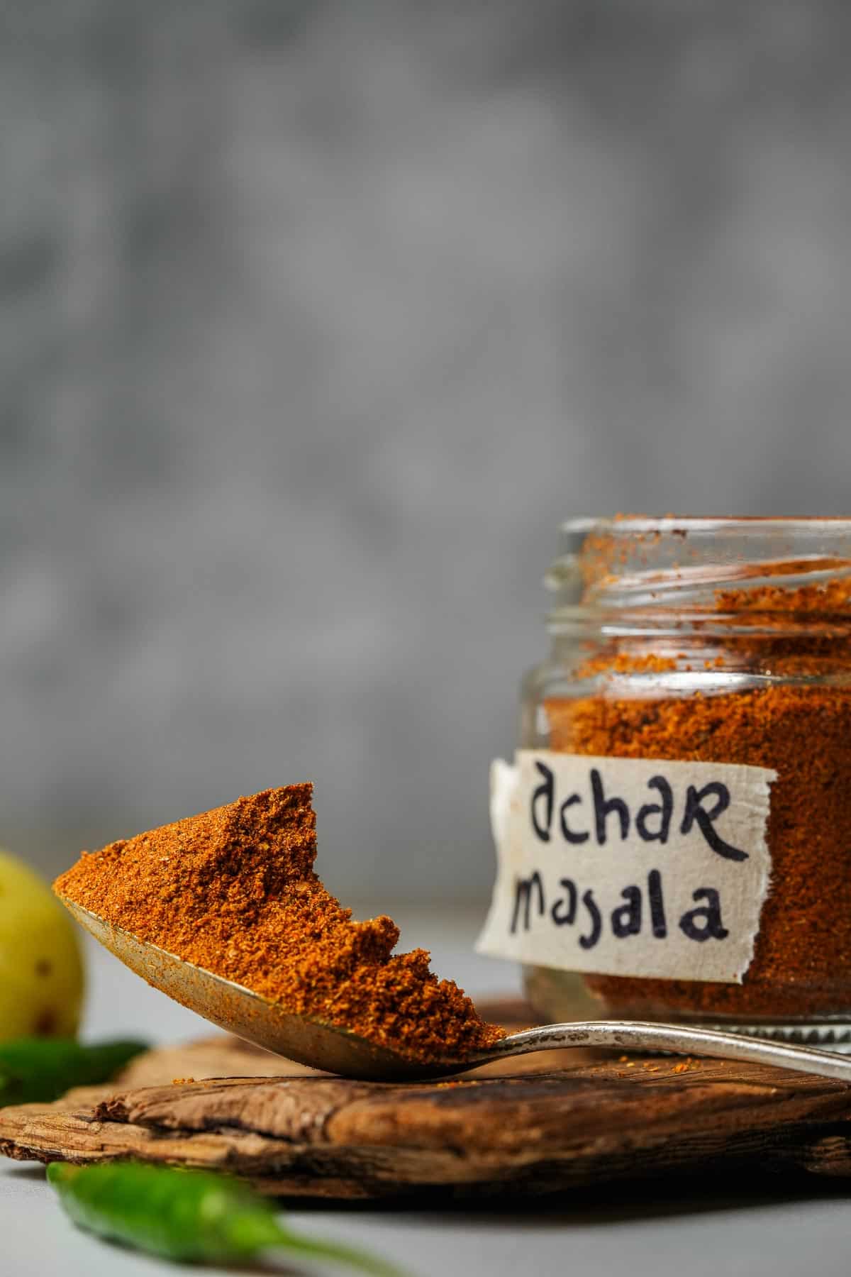 A jar of being filled with achar masala with a spoon.