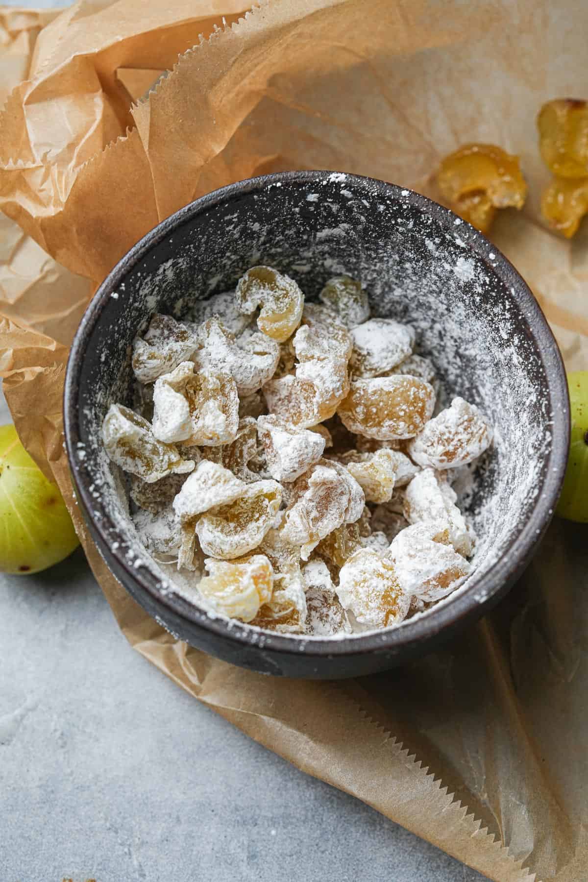 Candied amla coated in powdered sugar in a bowl.