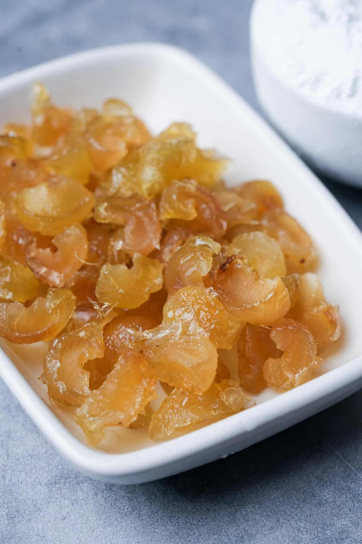 A white plate with a bowl of dried candied amla.