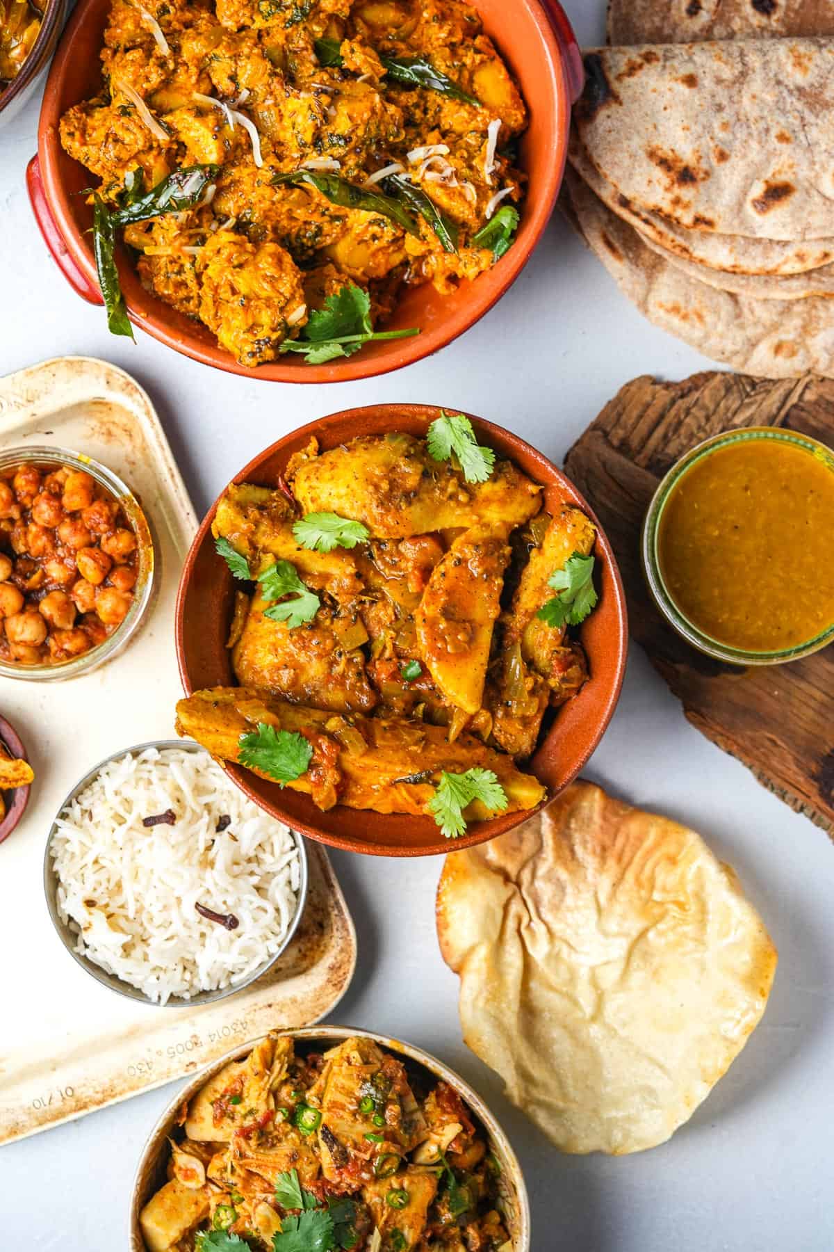 A variety of Indian food in bowls on a table including arbi ki sabji in a red bowl.