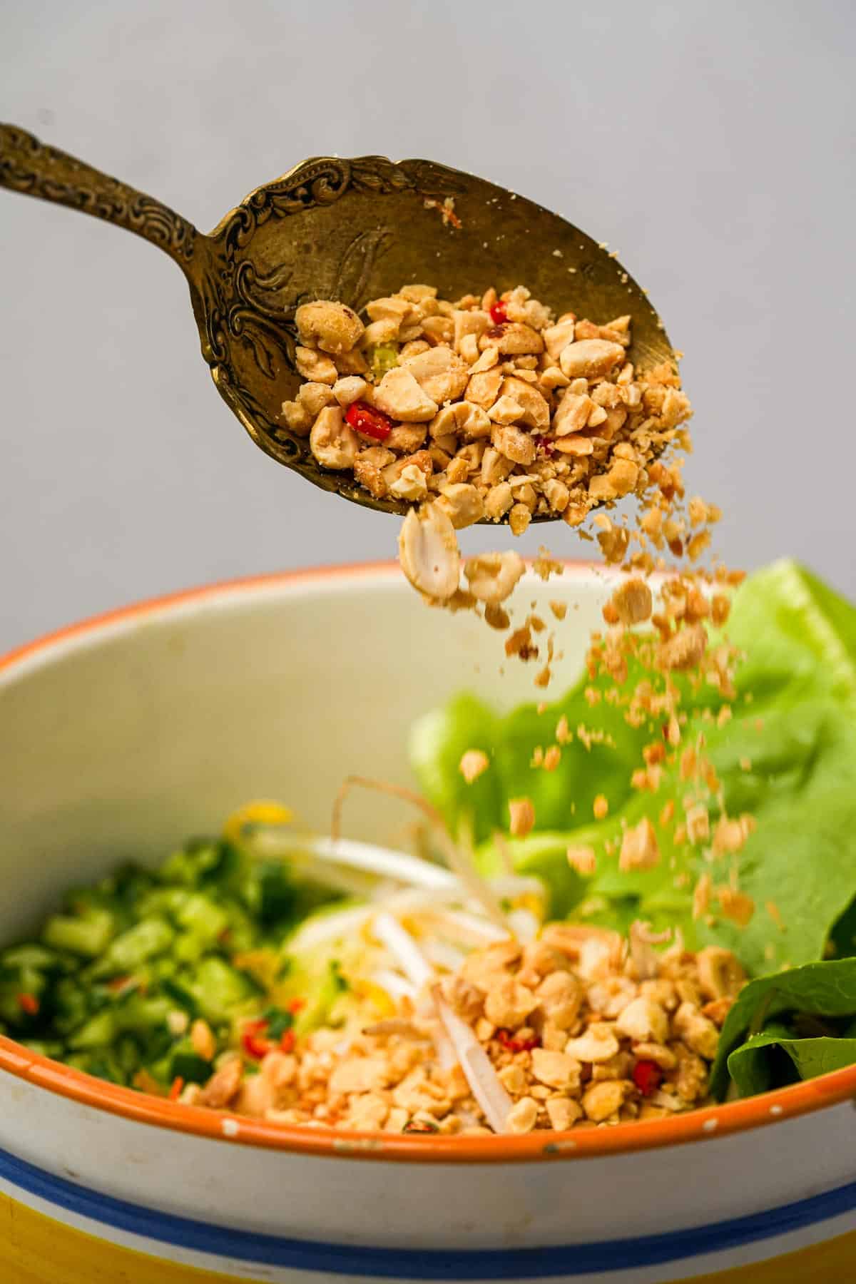 A spoon is sprinkling crushed peanuts on a bowl of salad.