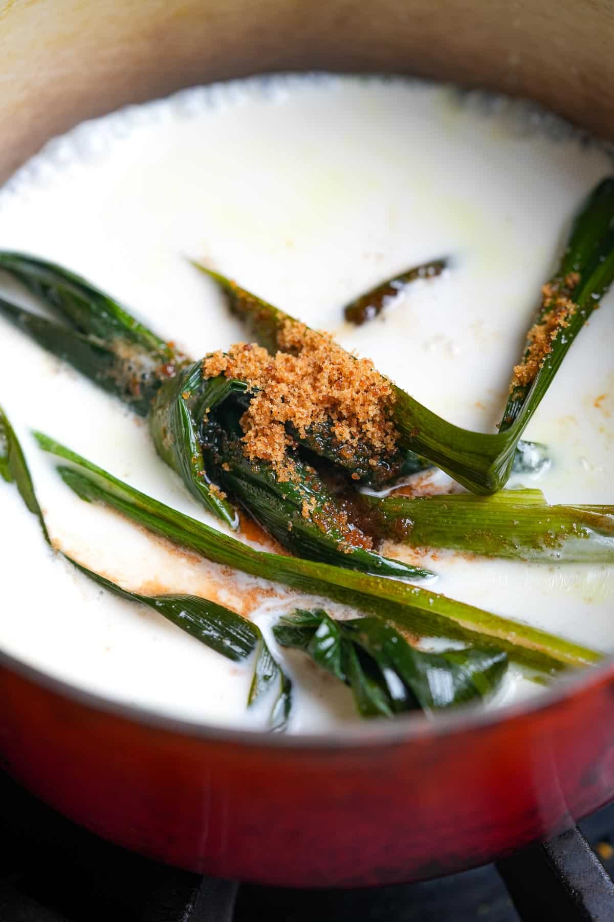 A pot filled with coconut milk, pandan and palm sugar on a stove.