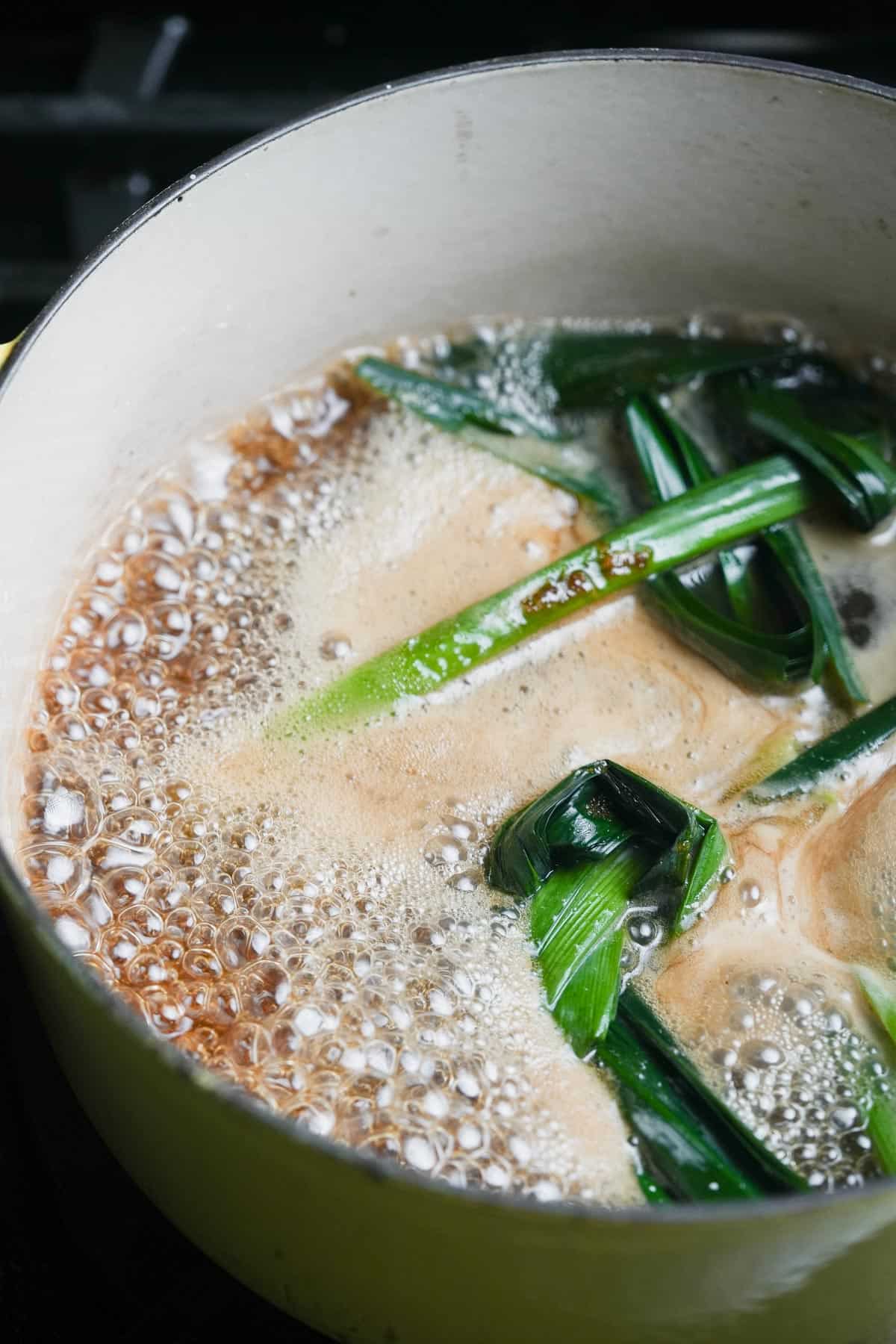 A pot filled with water and pandan leaves, boiling on a stove.