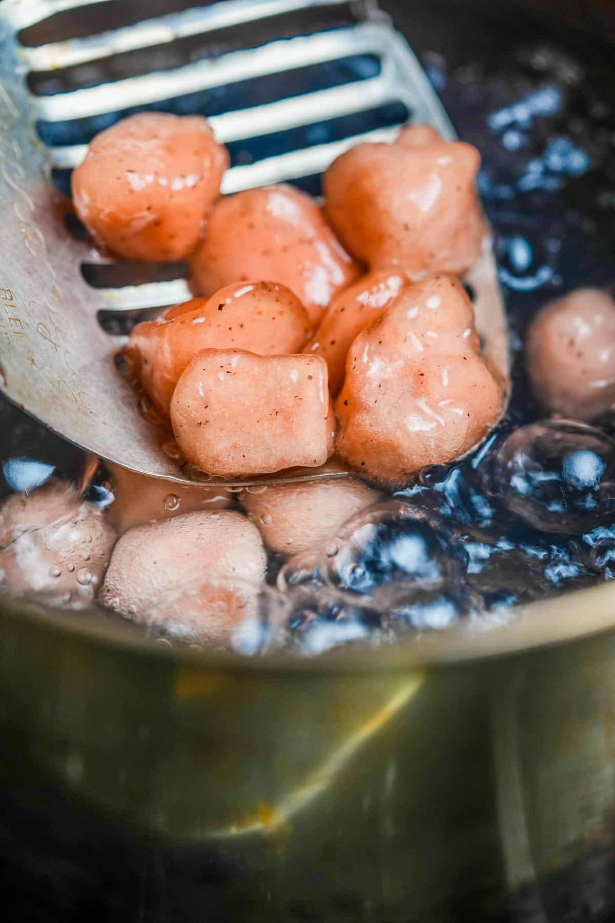 A metal slotted spoon is being used to removed cooked tapioca jellies from a pot of boiling water.