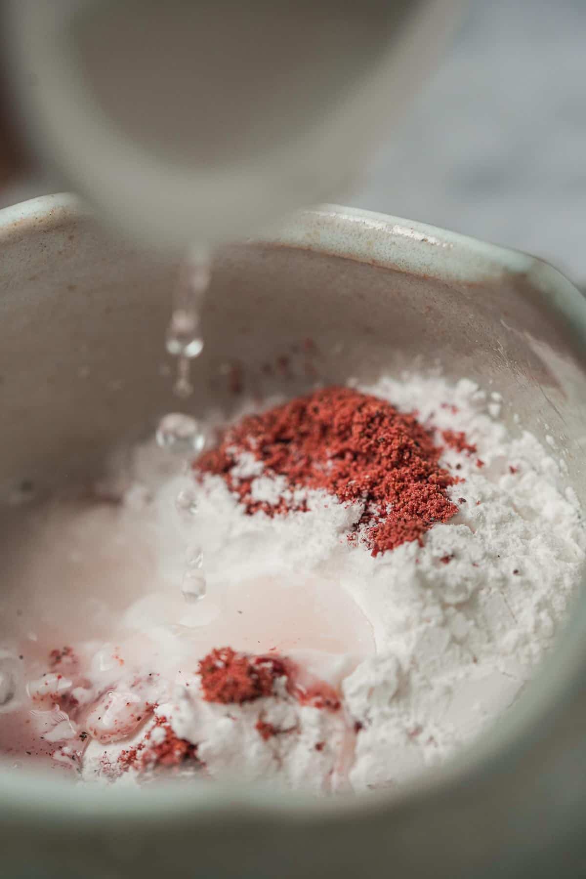A person is pouring boiling water into a bowl with tapioca starch and pitaya powder.