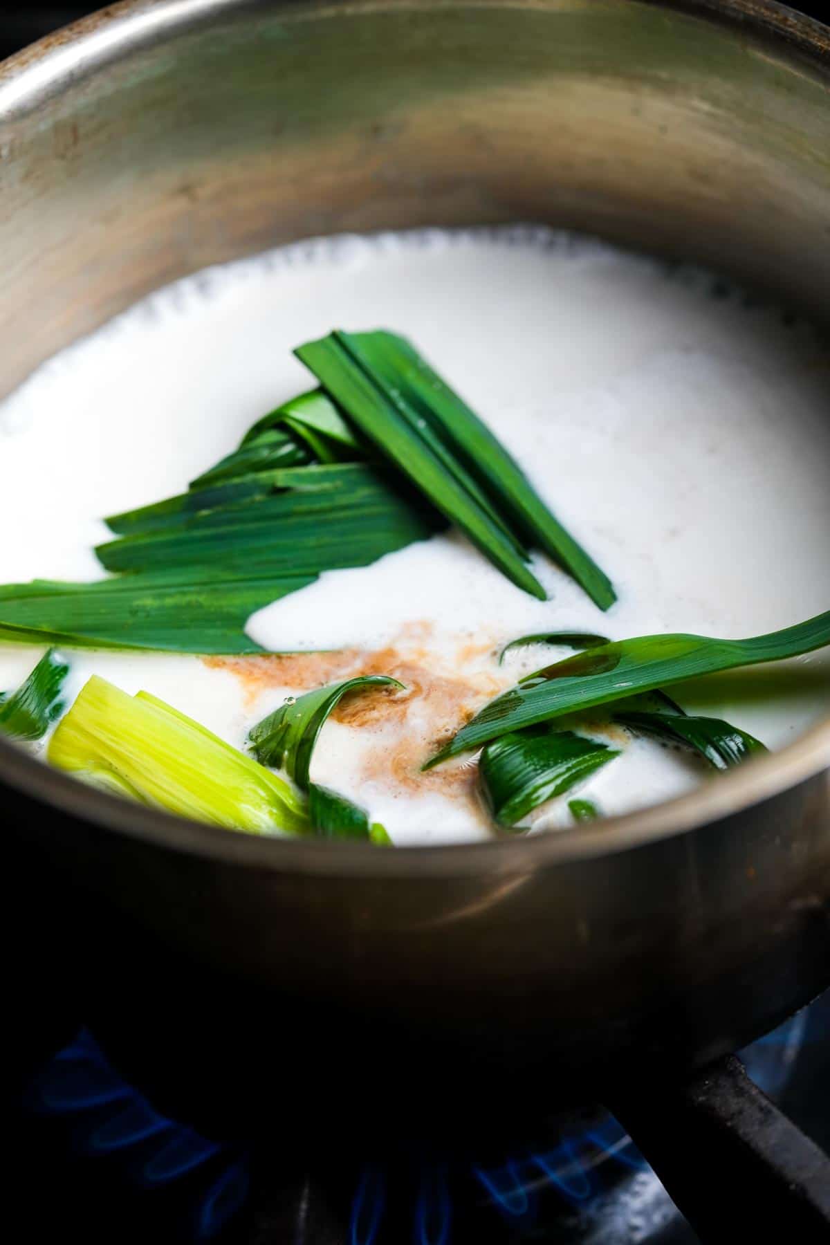 A pot with pandan leaves cooking in coconut milk on the stove.