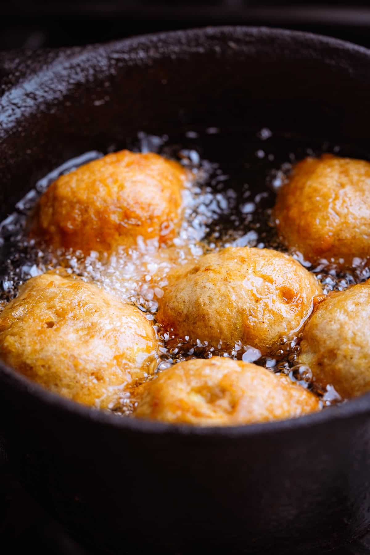 Fried balls of banana batter cooking in a cast iron pot of oil.