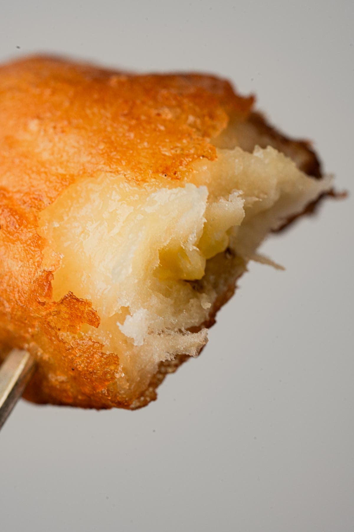 A fork is holding a piece of fried banana. Crispy and golden on the outside and fluffy and tender on the inside.
