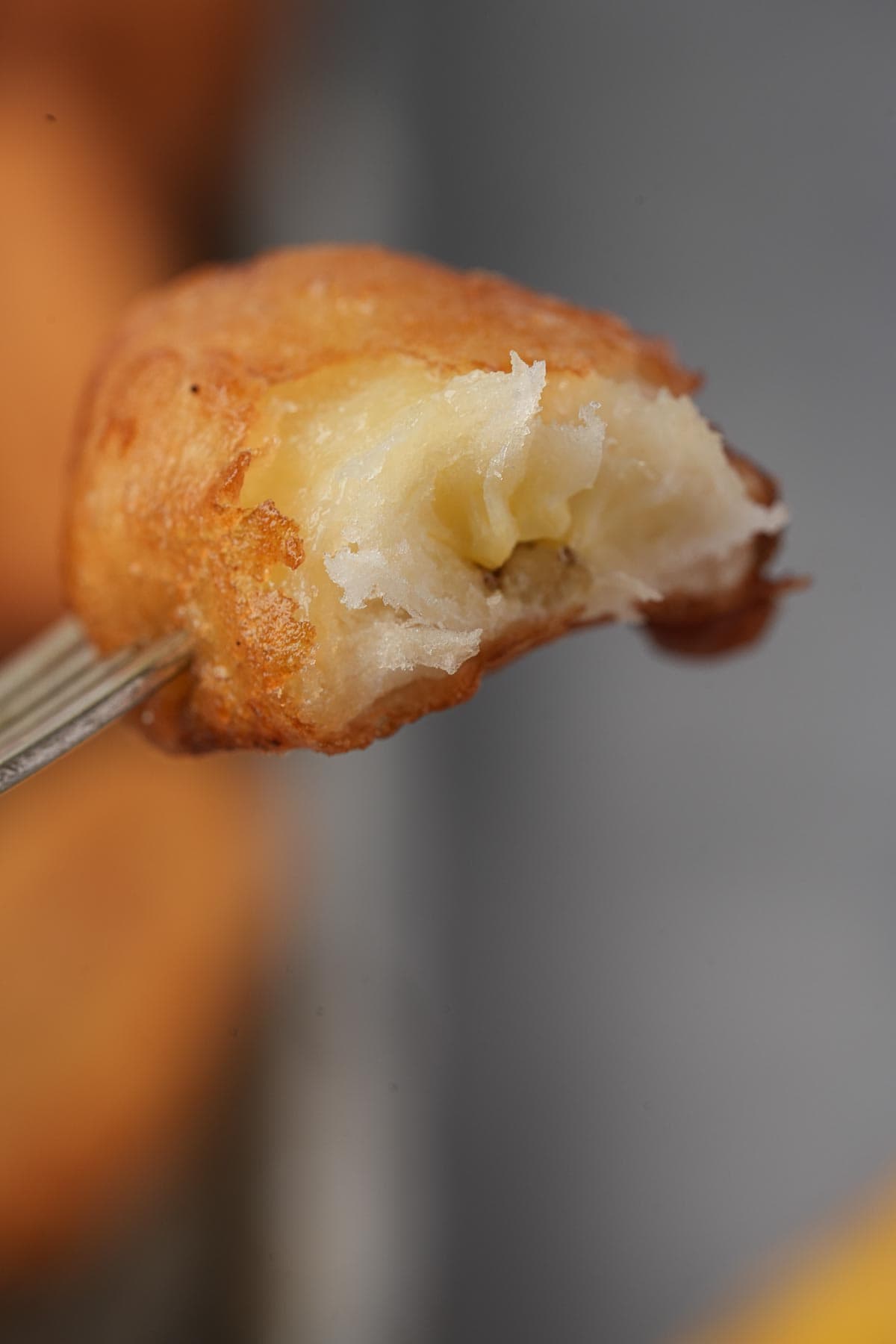 A fork is holding a piece of fried banana. Crispy and golden on the outside and fluffy and tender on the inside.