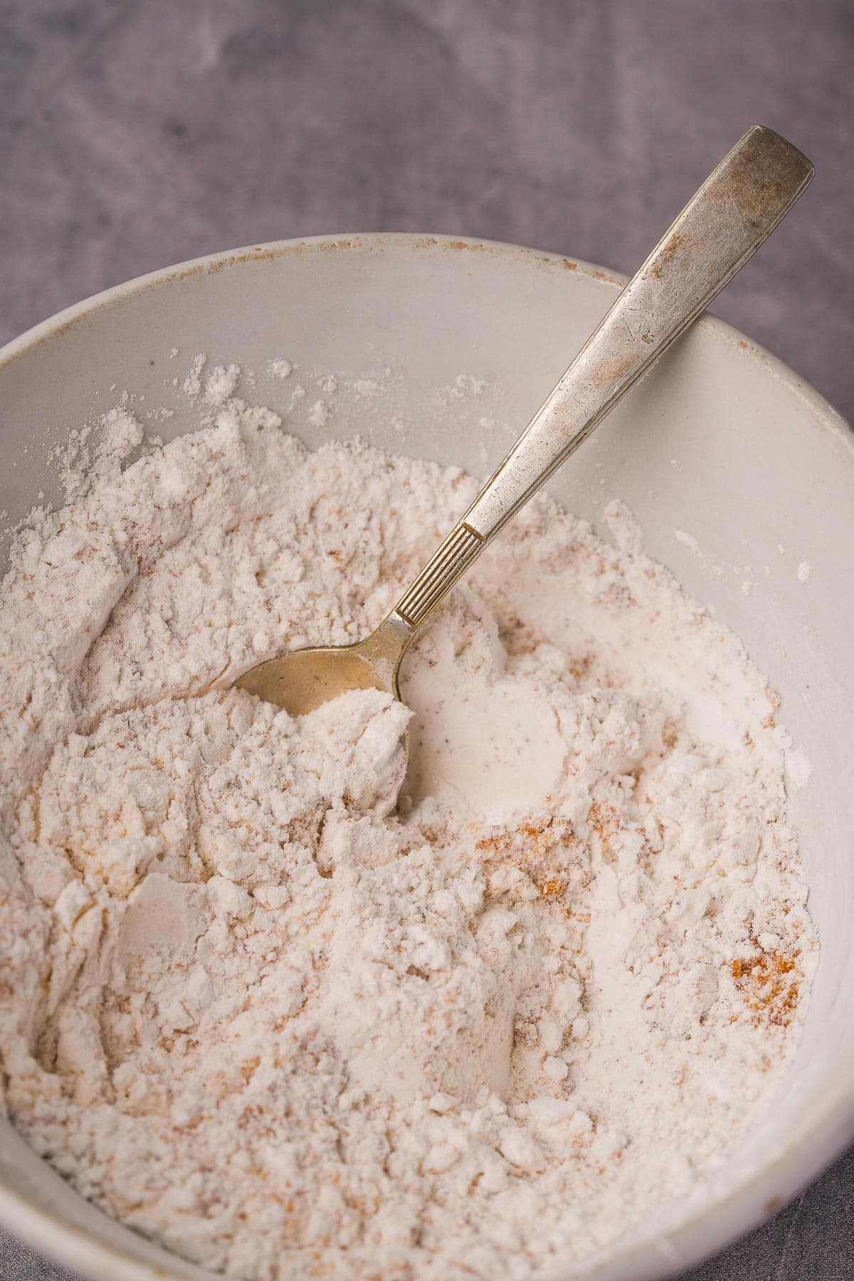 A bowl of flour with a spoon in it.