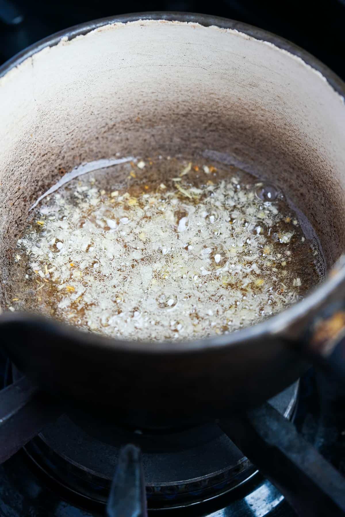 A saucepan on a stove with lemongrass and coconut oil in it.