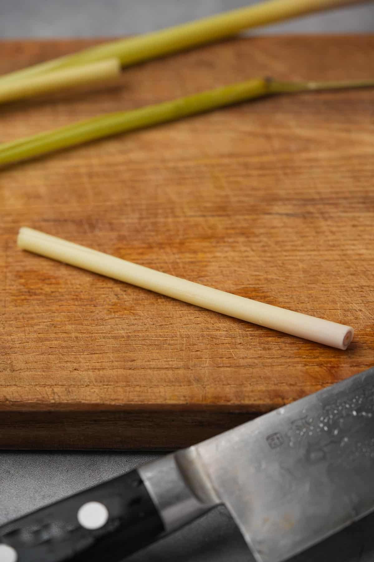A knife and a stick of lemon grass on a cutting board.