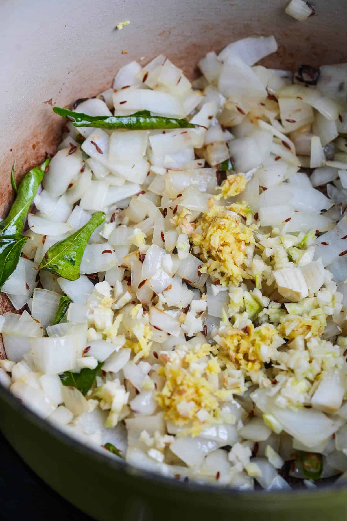 A pan filled with onions, cumin seeds, curry leaves, and ginger.