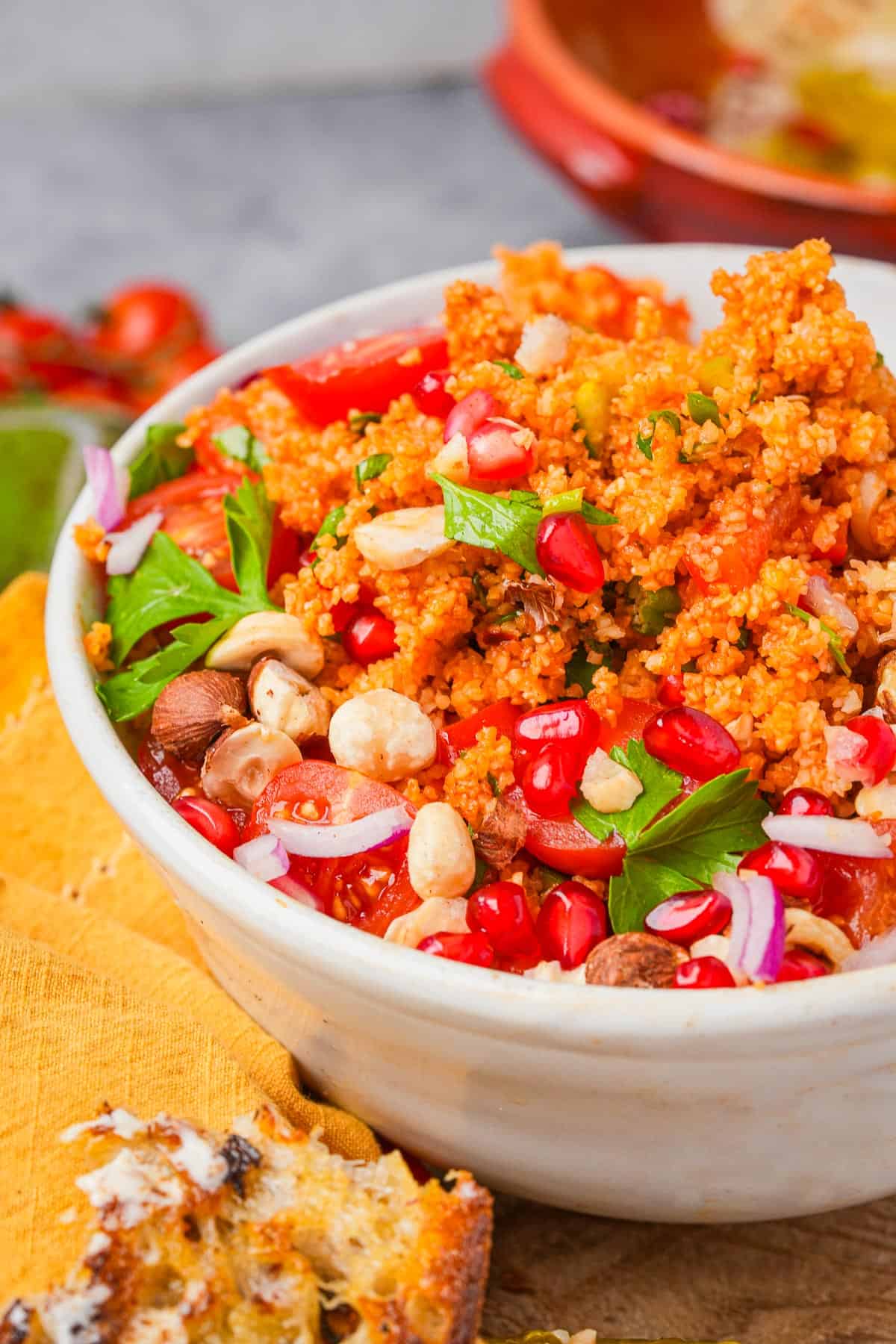 A bowl of kisir bulgur salad with tomatoes, herbs, pomegranate seeds, and nuts.